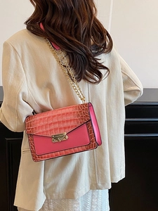 Pink crocodile-embossed crossbody bag with gold chain and metal buckle on model