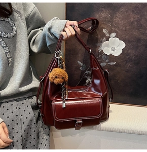 Detail of red-brown oil wax leather hobo bag with front buckle pocket and plush dog charm