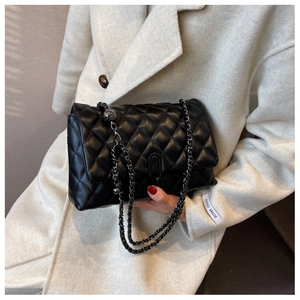 Detail of a black quilted crossbody bag with metal chain strap and U-shaped lock
