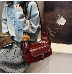 Close-up of wine red faux leather shoulder bag with a cute brown teddy bear plush charm
