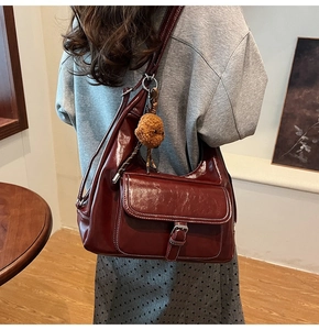 Detail of burgundy wax leather shoulder bag featuring silver buckle and white stitching