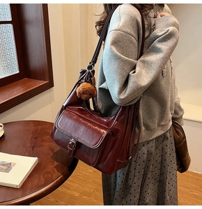 Detail of burgundy oil wax leather shoulder bag with buckle pocket and plush bear charm