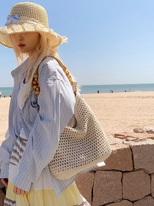 Handwoven beige crochet beach bag with wooden bead straps against a scenic seaside backdrop