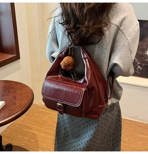 Detail of dark red oil wax leather shoulder bag with white stitching and bear charm