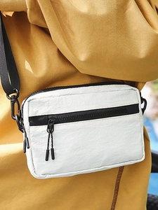 White textured nylon crossbody bag with black contrast zippers and adjustable strap