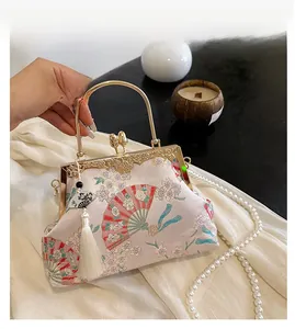 Detail of pink embroidered silk handbag with metal handle and elegant white tassel
