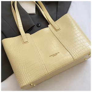 Détail du sac cabas beige gaufré crocodile avec pieds en métal doré et lettrage de marque