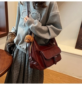 Detail of burgundy oil wax leather shoulder bag with white contrast stitching and teddy charm