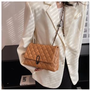 Caramel quilted chain bag detail with matte black clasp worn over a beige suit