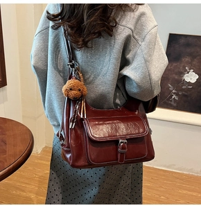 Close-up of a burgundy oil wax leather shoulder bag with a cute teddy bear charm