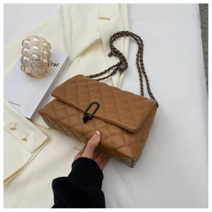 Detail of caramel quilted chain bag with black metal clasp and textured PU leather