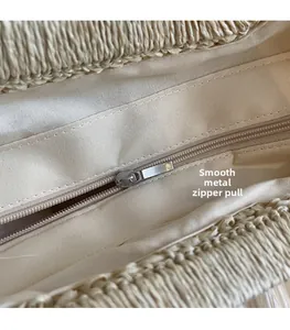 Detail of smooth metal zipper pull and beige fabric lining on woven beach bag