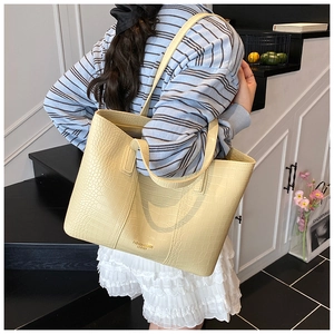 Détail d'un sac cabas jaune clair à motif crocodile avec lettrage doré sur le devant