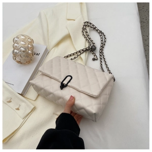 Close-up of beige quilted flap bag featuring unique black oval buckle and chain strap