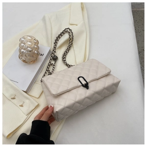 Detail of beige quilted shoulder bag with black metal clasp and chain strap on a blazer
