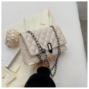 Detailed view of quilted cream chain bag with unique black metal clasp and decorative bead