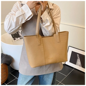 Gros plan d'un sac cabas beige à texture crocodile porté à l'épaule par un mannequin