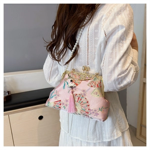 Model wearing a pink embroidered silk clutch bag with pearl strap and tassel detail