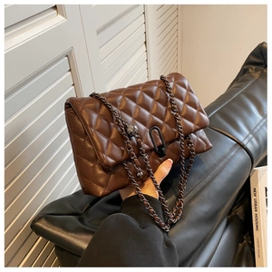 Detail of dark brown quilted crossbody bag with black metal lock and chain strap
