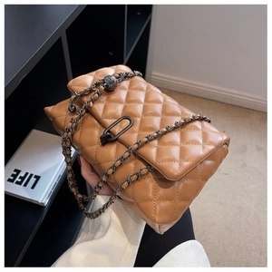 Detail of camel quilted leather shoulder bag with dark metal chain strap being held