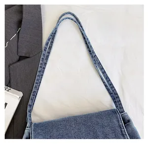 Détail du sac cabas en denim montrant la texture du tissu et les bretelles sur tissu blanc