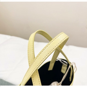 Detail view of light yellow bucket bag showing fine texture and silver metal hooks