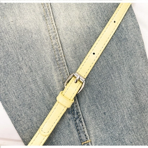 Detail of adjustable beige leather strap with silver buckle on blue denim bucket bag
