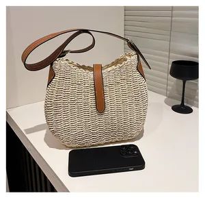 Sac à bandoulière en paille et cuir marron à côté d'un téléphone pour la taille