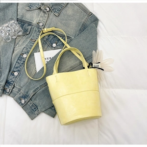 Detail of light yellow bucket bag with matte leather texture and white flower charm