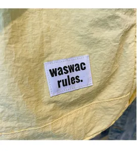 Detail of light yellow drawstring bag with waswac rules woven label and stitching