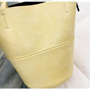 Detail of light yellow bucket bag featuring cracked texture and double stitching lines