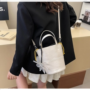 Close-up of cream bucket bag with yellow drawstring detail and floral charm accessory