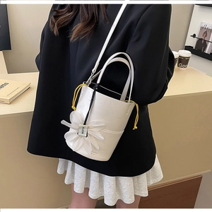Detail of white leather bucket bag featuring a 3D flower charm and yellow drawstring closure
