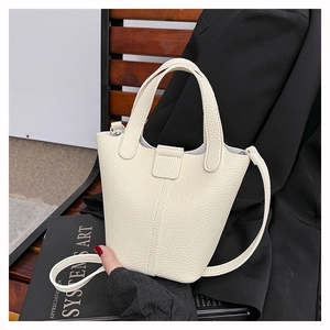 Detail of cream white leather bucket bag with litchi texture on a minimalist wooden bench