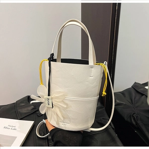 Close-up of white leather bucket bag with floral charm and yellow drawstring detail