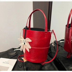 Detail of red bucket bag in glossy wrinkled leather with flower charm on dark coat