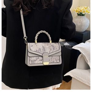 Detail of grey crossbody bag with traditional embroidery and braided handle texture