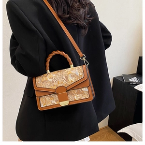 Detail of vintage brown leather bag with floral pattern, woven handle and gold lock