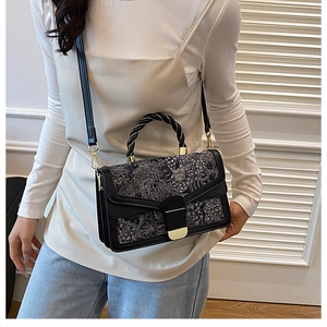 Close-up of black floral jacquard shoulder bag with gold clasp and twisted handle detail