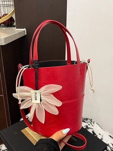 Red textured bucket bag with large white flower charm and adjustable crossbody strap