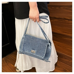 Détail du sac bandoulière en denim bleu clair avec fermoir rotatif argenté et boucle
