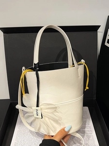 White leather bucket bag with yellow drawstring and flower charm in minimalist gift box