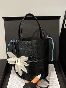 Chic black bucket bag with glossy pleated texture and floral charm in a gift box