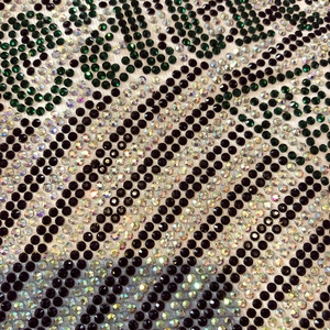 Detailed close-up of intricate rhinestone pattern with green and black crystals on cotton fabric