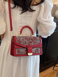 Elegant red shoulder bag with white floral embroidery and woven handle worn by a model