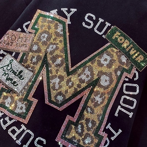 Gros plan de strass à motif léopard formant un M sur un t-shirt noir en coton haut de gamme