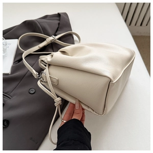 Close-up of cream lychee leather cloud bag with pleated details on a grey blazer