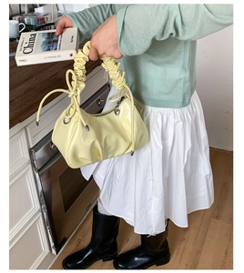 Détail d'un sac à main jaune crème en cuir verni avec anse froncée et pendentif cœur