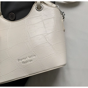 Detail of white crocodile embossed texture on a bucket bag with silver metal eyelets