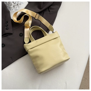 Dettaglio di una borsa a secchiello beige trapuntata con tracolla larga in tessuto su abito